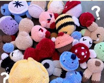 May include: A collection of colorful, handmade crochet items, including a turtle, bee, mushroom, and other plush figures. The text "Mystery Crochet Bag" is displayed at the top, with question marks scattered throughout the image.