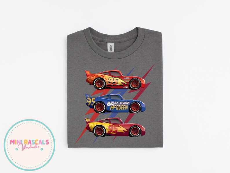Puede incluir: Una camiseta gris con tres coches de carreras de dibujos animados en rojo, azul y amarillo. Cada coche tiene el n&uacute;mero 95. El coche azul tiene el texto "Fabulous Lightning McQueen". Rayos rojos detr&aacute;s de los coches.