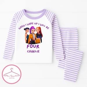 May include: A white and lavender striped pajama set for children. The long-sleeved top features a graphic of three cartoon girls and the text "WHEN I WAKE UP I WILL BE FOUR CHARLIE". The matching pants are also striped.