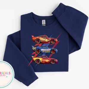 Puede incluir: Sudadera azul marino de manga larga con tres coches de carreras. Los coches, rojos, azules y amarillos, llevan el n&uacute;mero 95. El coche azul tiene el texto "Fabulous Lightning McQueen".