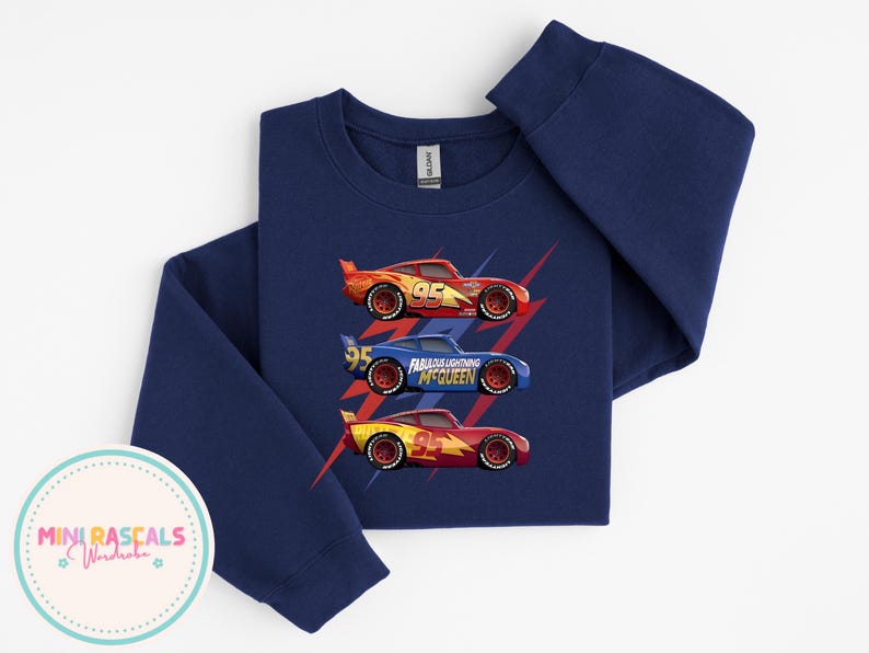 Puede incluir: Sudadera azul marino de manga larga con tres coches de carreras. Los coches, rojos, azules y amarillos, llevan el n&uacute;mero 95. El coche azul tiene el texto "Fabulous Lightning McQueen".