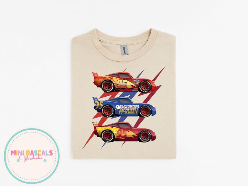 Puede incluir: Una camiseta beige con tres coches de carreras de dibujos animados en rojo, azul y amarillo. Cada coche tiene el n&uacute;mero 95. El coche azul tiene el texto "Fabulous Lightning McQueen". Gr&aacute;ficos de rayos rojos y azules detr&aacute;s de los coches.