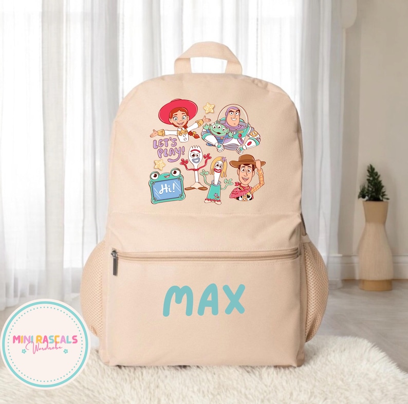 Puede incluir: Mochila beige con un dise&ntilde;o gr&aacute;fico colorido de personajes de dibujos animados. La mochila tiene un bolsillo frontal con cremallera y el nombre "MAX" en letras azules. Tambi&eacute;n tiene bolsillos laterales de malla y un asa superior.