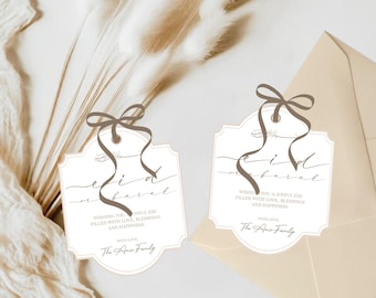 May include: Two white gift tags with brown ribbon bows and gold trim. The tags have the text "Eid Mubarak" written in calligraphy and a message wishing a joyful Eid filled with love, blessings, and happiness. The tags are signed "With Love, The Amir Family."