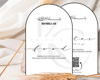 May include: Two white arch-shaped signs with black text. The top sign says "Bismillah" and the bottom sign says "Kairos & Food". The text on the bottom sign is in a cursive font. The sign also says "Break your fast and enjoy! May Allah accept your fast and prayers". The second sign says "Kairo & Co. Tarmees" and "Come and play! Engage on the Holy Month". A QR code is on the sign. The text "Scan Me!" is on the sign with a black arrow pointing to the QR code.