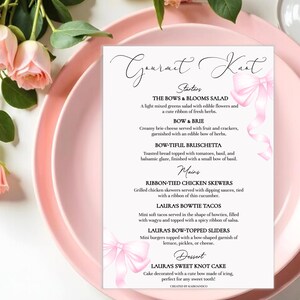 Può includere: Un biglietto menu rosa e bianco per un evento gourmet, con un design floreale e un motivo a fiocco. Il menu elenca antipasti, piatti principali e dessert, tra cui insalate, tacos e torte. Il biglietto è posto su un piatto rosa, con fiori rosa sullo sfondo.