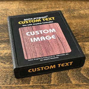 May include: A black rectangular video game cartridge featuring a label with the text game program CUSTOM TEXT Use with Joystick Controller. The center displays a wood grain pattern with CUSTOM IMAGE in white. The bottom edge reads CUSTOM TEXT.