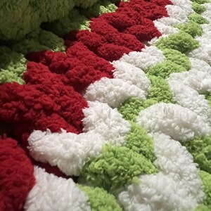 May include: A close-up of a fluffy, multi-coloured blanket with red, white and green stripes. The blanket is made of soft, textured yarn and has a unique, woven design.