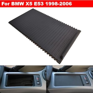 May include: A black, textured car console cover for a BMW X5 E53 model from 1998-2006. The cover has a ribbed design and is shown in the image with the console open and closed.