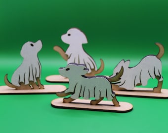 May include: Four wooden dog figurines in various poses, each with a light gray body, brown legs and tail, and a dark gray outline. The dogs are mounted on small, light brown wooden bases against a green background.