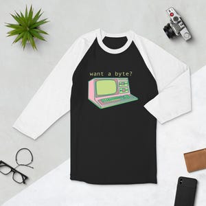May include: Black and white baseball tee shirt with a pink and green retro computer graphic and the text "want a byte?" printed on the front.