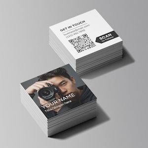 May include: Stacks of square business cards. One stack features a photograph of a person holding a camera, with the text "YOUR NAME" and "Title/slogan here." The other stack has contact information and a QR code with the text "GET IN TOUCH" and "SCAN to follow."