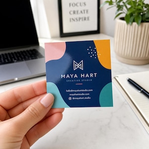 May include: A square business card with a dark blue center featuring the white logo and text MAYA HART CREATIVE STUDIO, surrounded by abstract shapes in pink, yellow, and teal. The card includes the email hello@mayahartstudio.com and website.