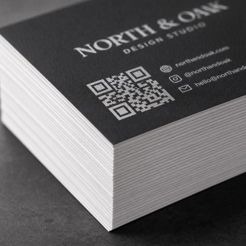 May include: A stack of rectangular business cards with a matte black finish and white text. The cards feature the text NORTH & OAK DESIGN STUDIO, a square QR code, and contact information including a website, Instagram handle, and email address.