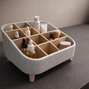 May include: A light gray, ribbed cosmetic organizer with wooden dividers and small wooden legs. The organizer is filled with various beauty products, including bottles, tubes, and brushes. The overall design is modern and minimalist.