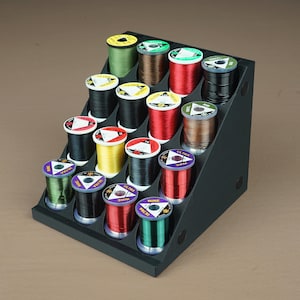 May include: A black triangular stand with 18 slots for spools of thread. The spools are in various colors, including green, red, yellow, brown, and black.