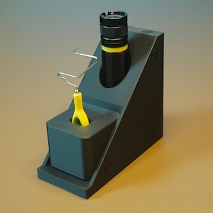May include: A black 3D printed stand with a yellow tool and a black flashlight. The stand has a slot for the flashlight and a hook for the tool.