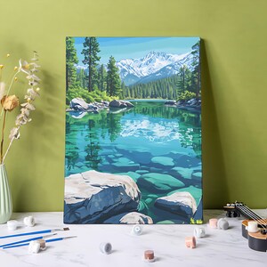 May include: A canvas print of a landscape painting showing a tranquil lake with clear turquoise water and large rocks. Green trees surround the shore, and snow-covered mountains are in the background under a blue sky. The artwork is displayed on a canvas.
