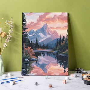 May include: A landscape painting depicts a mountain range reflected in a calm lake. The sky is filled with pink and orange clouds. The painting is surrounded by trees, and the scene evokes a sense of tranquility. Paintbrushes, paint pots, and a small ukulele are in the foreground.
