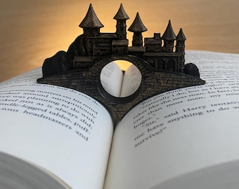 May include: A black 3D printed bookend shaped like a castle with a bridge. The bookend is holding open a book.