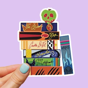May include: A stack of colorful stickers featuring stylized book spines. The spines are labeled with names like "The Queen," "Cruella De Vil," and "Maleficent." A green apple with a skull design sits atop the stack. The word "Hades" is on one spine.