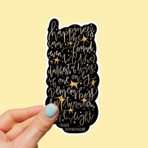 May include: A black sticker with gold lettering and star accents. The sticker features a quote by Albus Dumbledore: "Happiness can be found, even in the darkest of times, if one only remembers to turn on the light."
