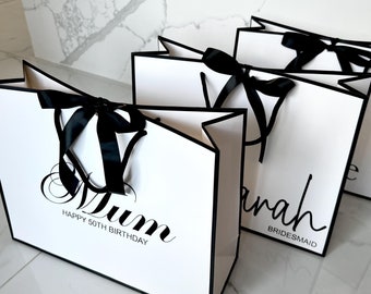 May include: Three white gift bags with black trim and black ribbon bows. The bags are labeled "Mum Happy 50th Birthday", "Sarah Bridesmaid", and "Bride".