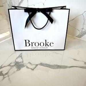 Personalised white gift bag featuring a custom name and decorative ribbon, great for bridal party presents