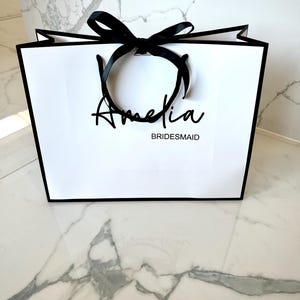 Personalised white gift bag with custom name, rope handles, and ribbon bow, ideal for birthday, wedding, or baby shower gifts