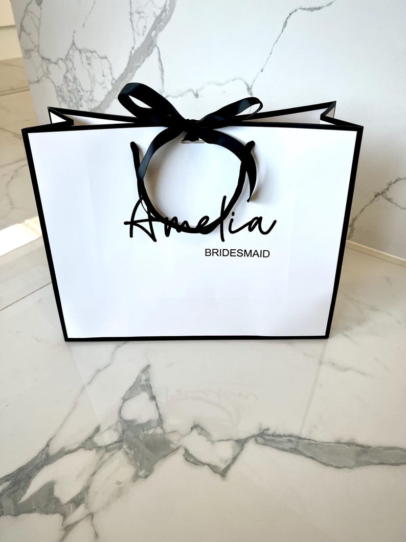 Personalised white gift bag with custom name, rope handles, and ribbon bow, ideal for birthday, wedding, or baby shower gifts