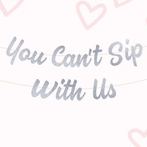 May include: A banner with the phrase "You Can't Sip With Us" in silver glitter lettering, strung across a white background. Light pink heart outlines are scattered around the edges, creating a festive design.