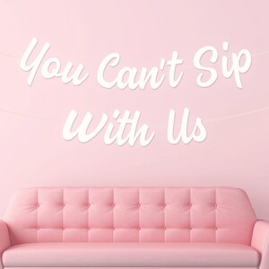 May include: A pink button-backed sofa is positioned beneath a banner with the white script text "You Can't Sip With Us". The background is a solid pink, with a white globe light on the right.