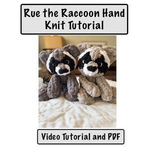 May include: Two gray and white crocheted raccoon hand puppets with black eyes and noses. The puppets are sitting on a white blanket. The text "Rue the Raccoon Hand Knit Tutorial" is at the top of the image and the text "Video Tutorial and PDF" is at the bottom of the image.