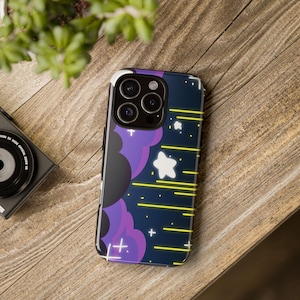 Puede incluir: Una funda de teléfono inteligente con un fondo azul oscuro que presenta un diseño de nube púrpura, estrellas blancas y líneas horizontales amarillas. La funda tiene un borde negro y está sobre una superficie de madera.