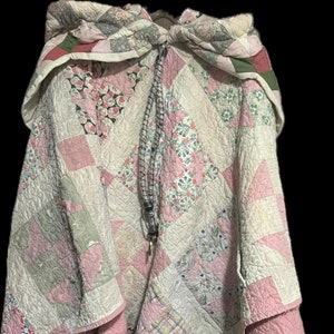 May include: A pink and white patchwork quilt with a hood. The quilt is made of various floral and geometric patterns.