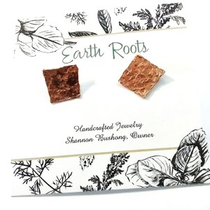 May include: Square copper earrings with a textured surface, displayed on a white card with the text "Earth Roots" and "Handcrafted Jewelry". The card has black and white botanical illustrations.