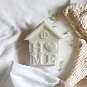 May include: White candle shaped like a house with the word "HOME" and two hearts on the front.