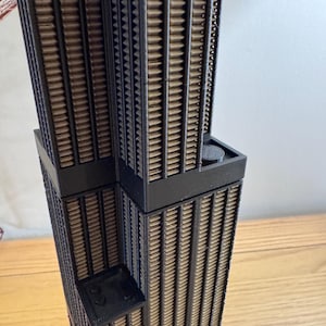 Puede incluir: Primer plano de una maqueta de rascacielos de color negro y marrón. La maqueta está hecha de cartón y tiene una fachada detallada.