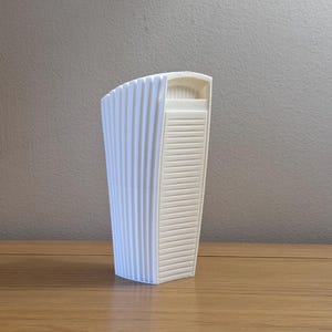 May include: White ceramic vase with a fluted design and a rectangular opening at the top.