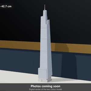 May include: A light gray architectural scale model of a skyscraper featuring a stepped, multi-tiered design with a central spire. The model is labeled with a 1:1000 scale and a height of 42.7 cm. The text "Photos coming soon" is visible below.