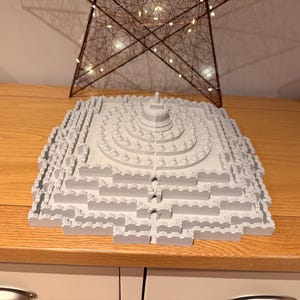 May include: A light grey 3D printed model of the Borobudur temple, featuring a square base with multiple stepped levels, a central stupa, and numerous smaller bell-shaped stupas arranged in concentric circles on the upper tiers of the structure.