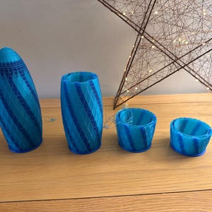 May include: Four blue and turquoise decorative vases with a striped pattern. The vases vary in size and shape, with one tall, one cylindrical, and two smaller, bowl-shaped designs. A star-shaped light fixture is in the background.