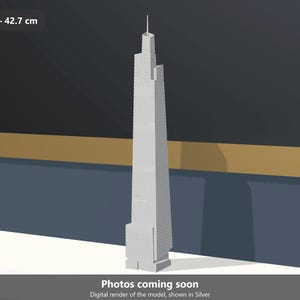 Könnte beinhalten: Ein silberfarbenes Architekturmodell des Willis Tower Wolkenkratzers. Das Modell zeigt ein gestuftes, mehrstöckiges Design mit einer zentralen Antenne an der Spitze. Ein Etikett gibt einen Maßstab von 1:1000 und eine Höhe von 42,7 cm an.