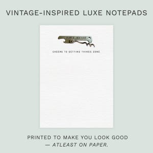 May include: A white notepad with a vintage-style corkscrew and the text "CHEERS TO GETTING THINGS DONE." The notepad is labeled "VINTAGE-INSPIRED LUXE NOTEPADS" and the bottom text reads "PRINTED TO MAKE YOU LOOK GOOD - ATLEAST ON PAPER."