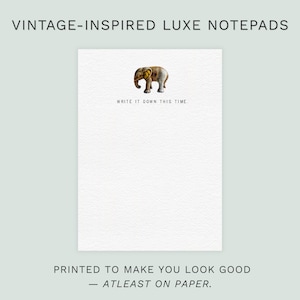 May include: A white notepad featuring a vintage elephant illustration. The text "WRITE IT DOWN THIS TIME" is below the elephant. The notepad is labeled "VINTAGE-INSPIRED LUXE NOTEPADS" and "PRINTED TO MAKE YOU LOOK GOOD - ATLEAST ON PAPER."