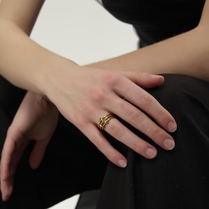 May include: A gold ring with a unique, interwoven design. The ring is worn on the index finger of a hand.