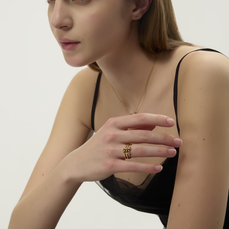 May include: A gold ring with a geometric design. The ring is worn on the index finger of a person's hand.