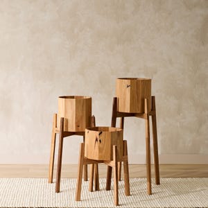 May include: Three wooden plant stands with round wooden planters. The stands are made of natural wood and have a simple, modern design.