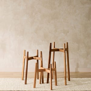 May include: Three wooden plant stands of varying sizes. The stands are made of natural wood and have a simple, rustic design. They are perfect for displaying plants or other decorative items.