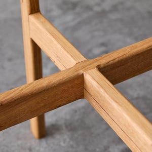 May include: Close-up of a wooden table base with a cross-shaped design. The wood is a light brown color and has a natural grain pattern.